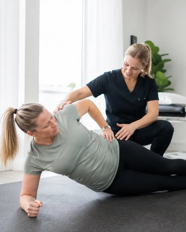 Fysioterapeutti ohjaa asiakkaan liikettä vastaanoton lattialla.